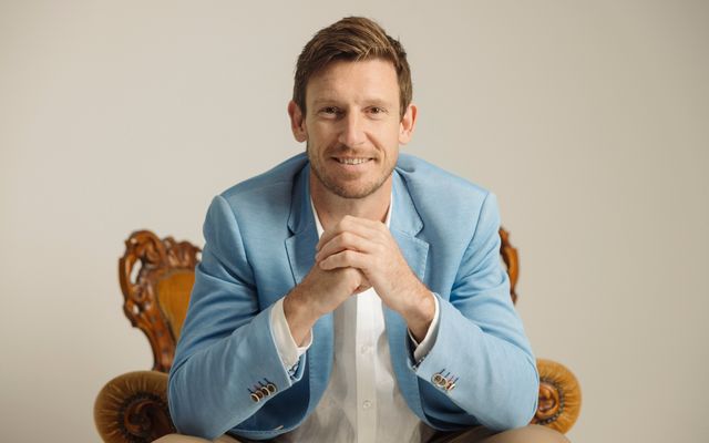 Mat Bankes seated in a carved timber chair, leaning forward with his hands clasped, smiling