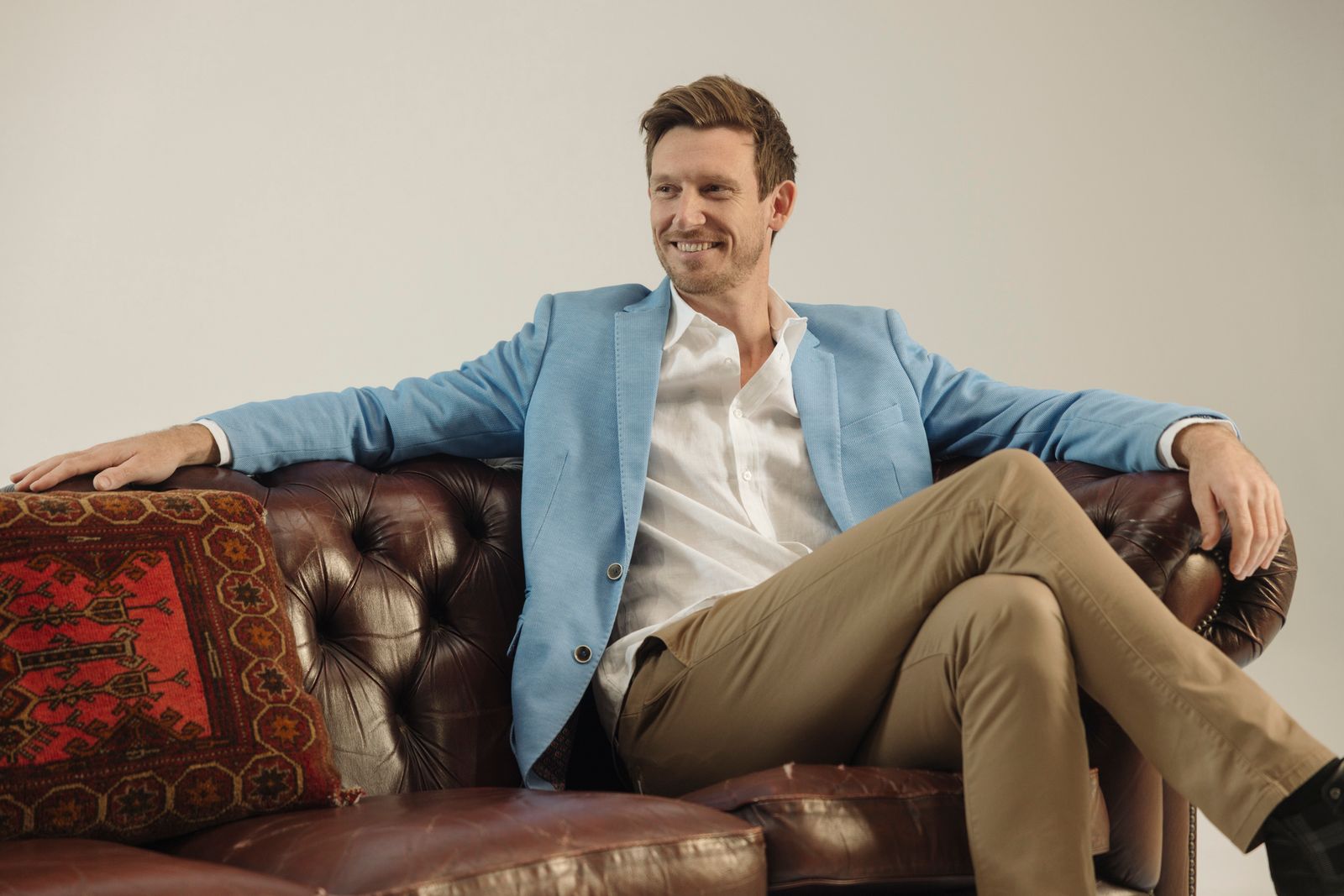 Mat Bankes relaxed on a leather couch, one arm along the back, smiling