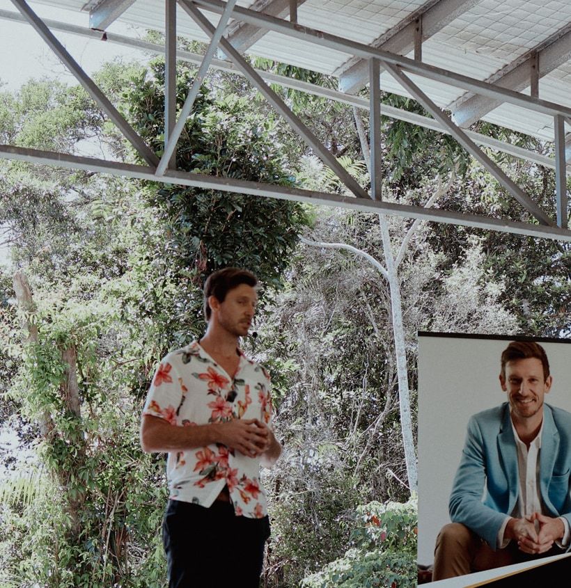 Mat Bankes speaking on the open-air stage at Connect Fest, Cairns, with rainforest behind him